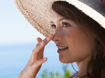 woman applying sunscreen outdoors with a straw hat